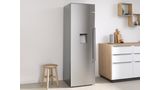 Серебряный отдельностоящий холодильник Bosch между маленьким табуретом слева и кухонной столешницей справа.