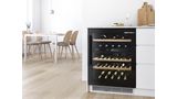 Шкаф Bosch для хранения и охлаждения вина со стеклянными дверцами демонстрирует коллекцию вина. Современный и светлый обеденный зал слева.