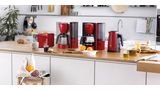 Zestaw ComfortLine w kolorze czerwonym i ze stali szlachetnej obejmujący toster, ekspres przelewowy do kawy i czajnik. Wiele składników śniadaniowych znajduje się na stole