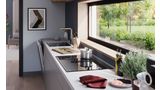 Schuin perspectief van een keukenopstelling onder een raam met een Bosch kookplaat met geïntegreerde afzuigmodule.