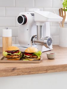 Two freshly made burgers next to a Bosch stand mixer with a meat mincer.