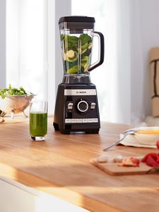 Liquidificador de alta velocidade VitaBoost cheia de frutas verdes e legumes na mesa da cozinha.