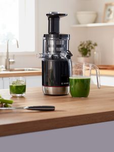 VitaExtract slow juicer placed together with juice jug and glass on kitchen table.