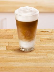 Sklenená šálka naplnená kávou „Latte Machiatto“.