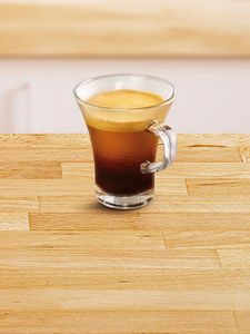 Malá sklenená šálka naplnená kávou „caffé lungo“.
