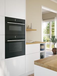 In einer hellen modernen Küche sind eine Mikrowelle und Herd untereinander in einem weißen Küchenschrank eingebaut.