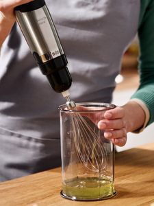 Eine Person verwendet einen Stabmixer mit Rührbesen, um Eiweiß in einem Mixbecher zu aufzuschlagen.