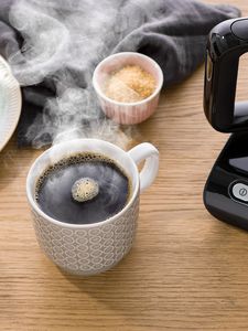 Hot mug of black coffee next to coffee machine on countertop
