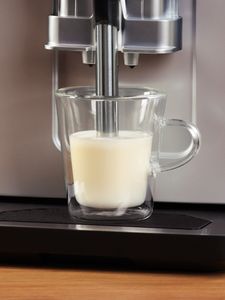 1 tejjel töltött csésze, lenyomott habosító karral, a Series 2 VeroCafe gép csepptálcájára helyezve.