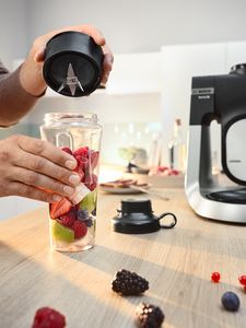 Imagine care prezintă sticla ToGo umplută cu fructe feliate, lângă un capac şi robotul Serie 6 aşezat pe blatul din bucătărie.