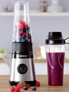 Bosch Miniblender VitaPower Series 2 ja punaisia hedelmiä sekä smoothiella täytetty ToGo-pullo keittiön hyllyllä.