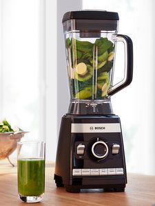VitaBoost high speed blender filled with green fruit and vegetables placed on kitchen table.