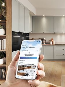 Een persoon houdt een telefoon vast, kijkend naar het scherm van Home Connect, met op de achtergrond een gezellige keuken.
