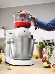 Vit Serie 6 köksmaskin med citruspresstillbehör och hand som pressar en rosa grapefrukt.
