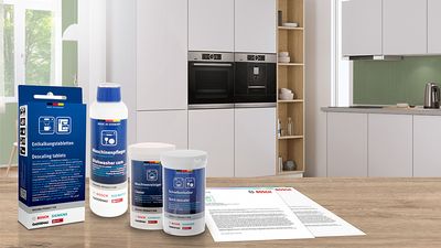 Rôzne produkty na čistenie a údržbu Bosch a dokumenty na bielom stole v otvorenej kuchyni.