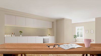 Óculos, manual do utilizador e copo sobre uma mesa branca e cozinha branca ao fundo.