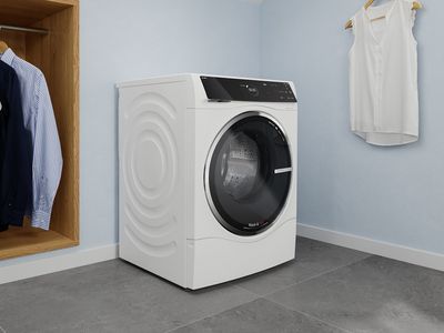 En vaske-/tørremaskine står i et lyst vaskerum ved siden af et åbent garderobeskab med nyvaskede skjorter.