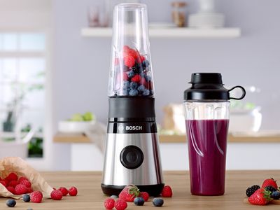 Миниблендерът на Bosch VitaPower Серия 2 с червени плодове и пълна със смути бутилка To-Go върху кухненски рафт.