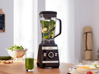 Bosch High Performance Blender VitaBoost Series 6 with fruits and vegetables and a smoothie glass on a kitchen shelf.