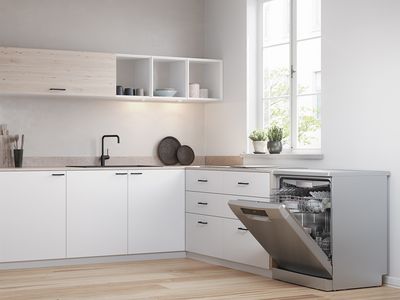 An open freestanding dishwasher in a white and bright kitchen.