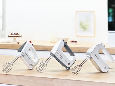 Drei Bosch Handrührer nebeneinander aufgereiht auf einer Küchenarbeitsplatte aus Holz.