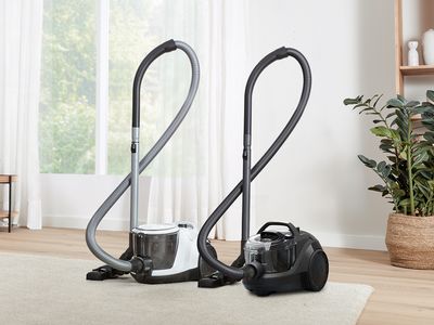 Two Bosch bagless cylinder vacuums stand on a cream rug in a light, bright living room.