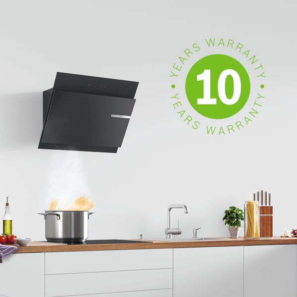 Hotte aspirante Bosch noire dans une cuisine blanche. Les pâtes cuisent sur une plaque à induction. L'icône de garantie de 10 ans à gauche indique une couverture de garantie étendue.