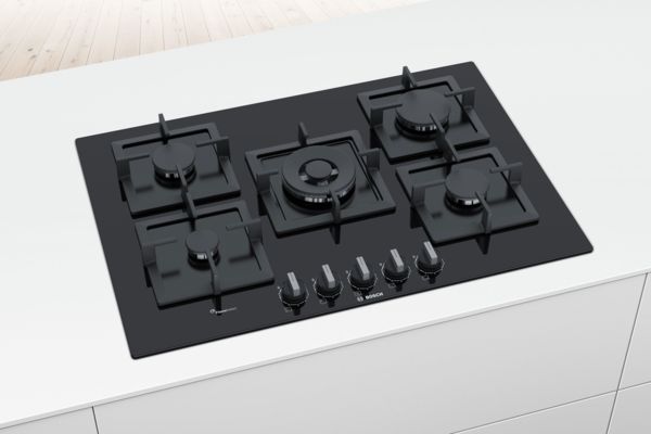Placa de vitrocerâmica preta Series 6 da Bosch com 5 queimadores numa ilha branca.