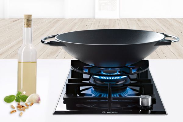 Piano cottura a gas Domino Bosch con bruciatore wok a doppia fiamma. Un wok appoggiato su un anello di supporto per wok, un accessorio Bosch.