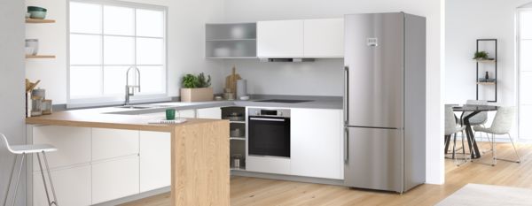 Просторная кухня со встраиваемым серебристым холодильником Bosch. Современная столовая на фоне.