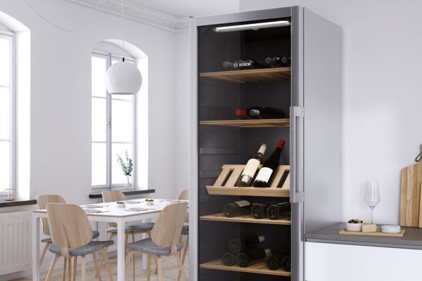 Винный шкаф Bosch со стеклянной дверцей демонстрирует коллекцию вин. Современная светлая столовая слева.