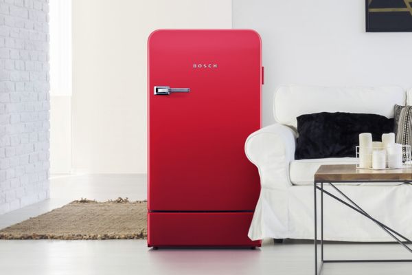 Красный отдельностоящий холодильник Bosch в современном помещении возле дивана и журнального столика.