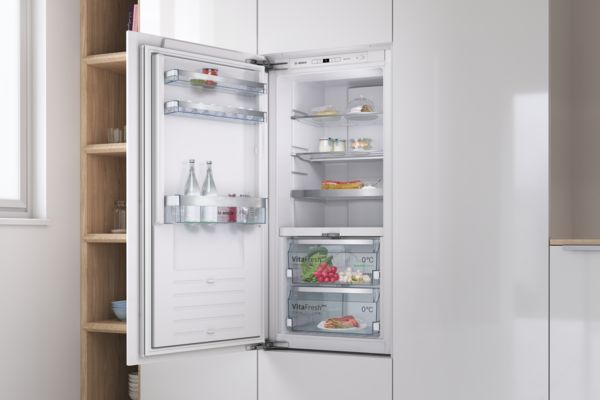 Встраиваемый холодильник Bosch с открытой дверцей, показывает продукты и напитки внутри. 