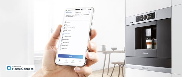 Smartphone, auf dem die Home Connect App geöffnet ist, und eine Auswahl verschiedener Kaffeespezialitäten, Kaffeemaschine von Bosch im Hintergrund. 