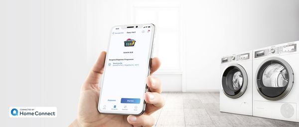 Home Connect App zeigt das empfohlene Waschprogramm an – Waschmaschine und Wäschetrockner von Bosch im Hintergrund. 