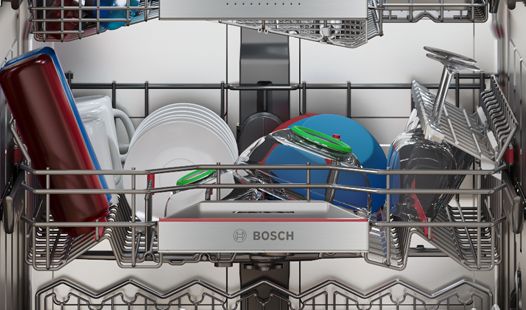 Nykyaikainen keittiö, jossa puulattiat, avoin Bosch-astianpesukone täynnä puhtaita jalallisia laseja, muoviastioita, kuppeja ja lautasia