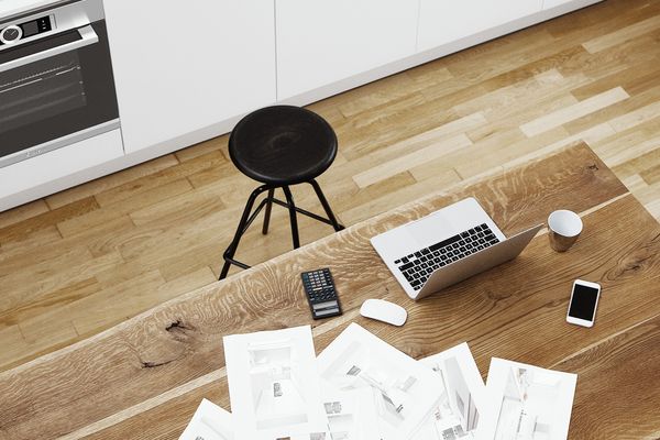 Laptop op een ruime keukentafel naast een stapel papieren met keukenontwerpideeën