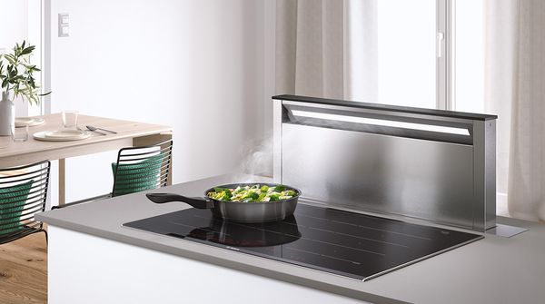 Daudz vietas ēdiena gatavošanai: liela indukcijas gatavošanas virsma, kas apvienota ar lejupvilkmes ventilāciju mājīgā virtuvē ar ēdamgaldu
