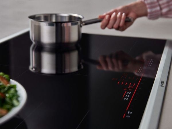Sleek built-in 60-centimetre electric cooktop in dark black glass with a stainless steel pot at the far corner