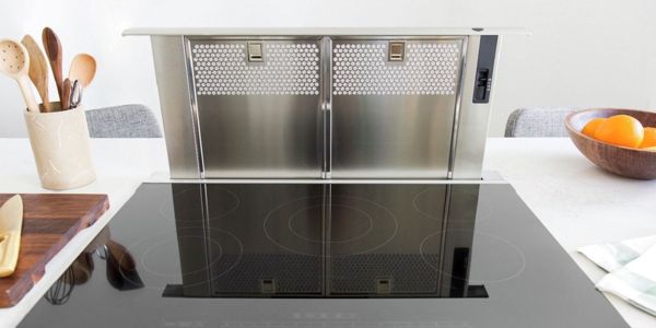 Stainless steel downdraft hood on a counter next to cooking utensils and fresh fruit
