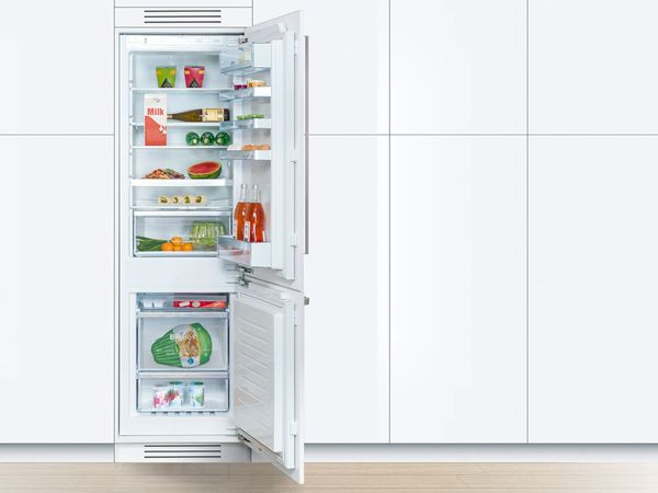 Compact stainless steel fridge freezer in a tiny kitchen with beige cabinets and stainless steel hardware