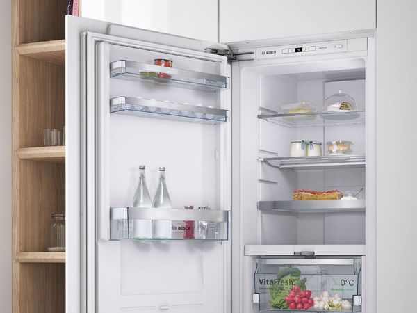 Balts ledusskapis bez saldētavas ar mājās gatavotiem piena produktiem ekoloģiski draudzīgos stikla traukos, svaigiem dārzeņiem un gardu zemeņu pīrāgu