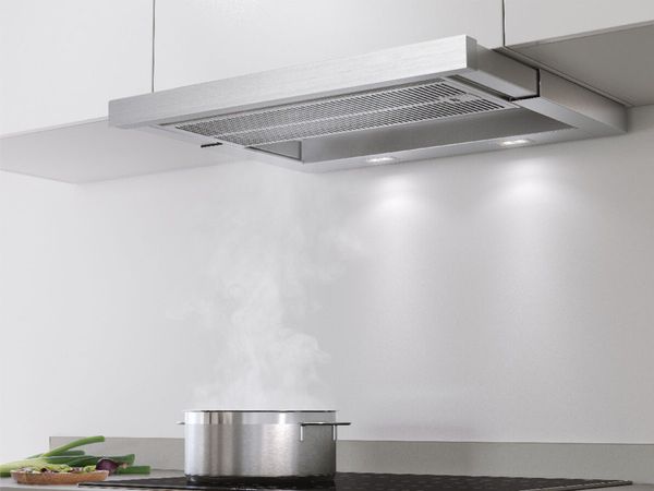 Bosch telescopic hood installed below cabinets absorbing steam from boiling water on the hob next to fresh veggies waiting to be added to the pot