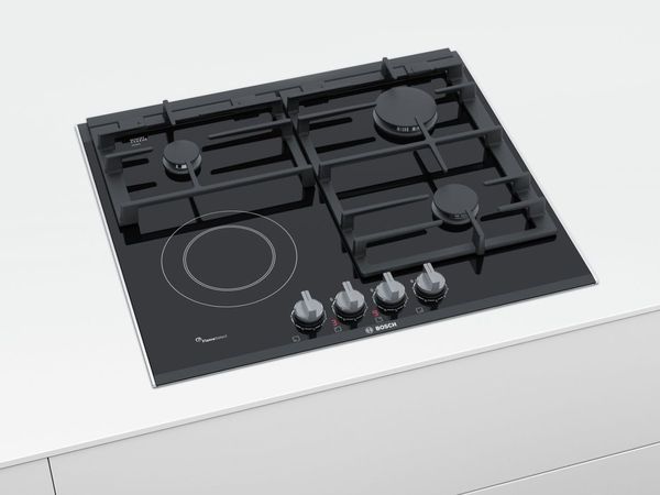Black mixed hob with three different sizes of gas burners and one ceramic glass dual ring burner on a white kitchen counter