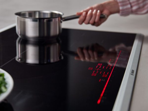 Built-in 24" electric cooktop in black glass with a stainless steel pot at the far corner