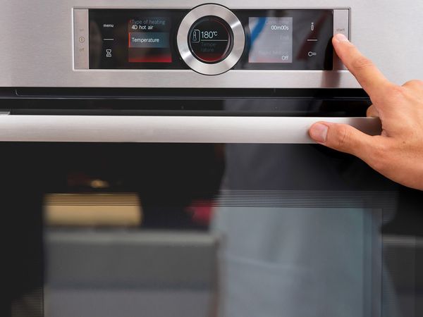 Mâna unui utilizator lângă butoanele de pe un panou de control al unui cuptor încorporabil cu programe diferite de coacere