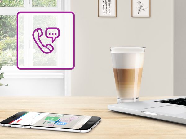 Laptop, telefon i kawa na stole kuchennym z fioletową ikoną obsługi klienta.