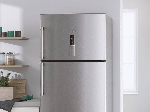 Stainless steel fridge with top freezer next to a white countertop with green accessories