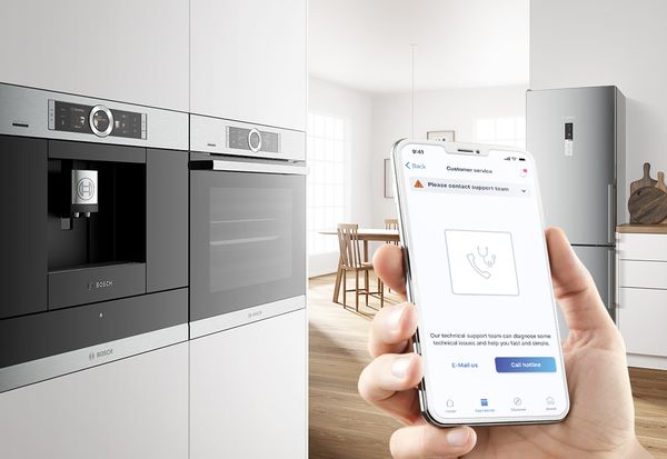 Smartphone met Home Connect app, Bosch oven en koffiemachine op de achtergrond.  