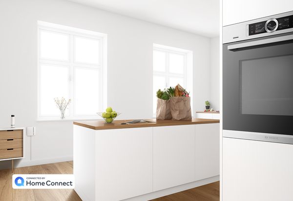 Модерна бяла кухня с домакински уреди Bosch и торби с хранителни стоки на кухненския остров.